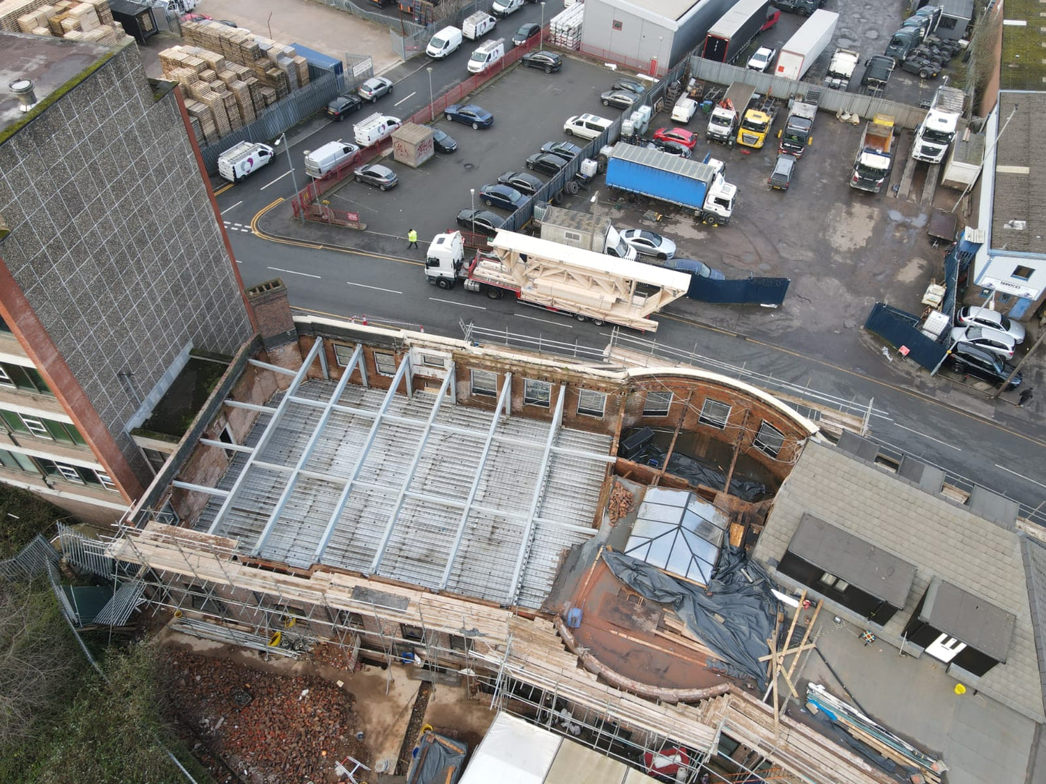 birds eye view of a building without a roof and a lorry delivering roof trusses behind