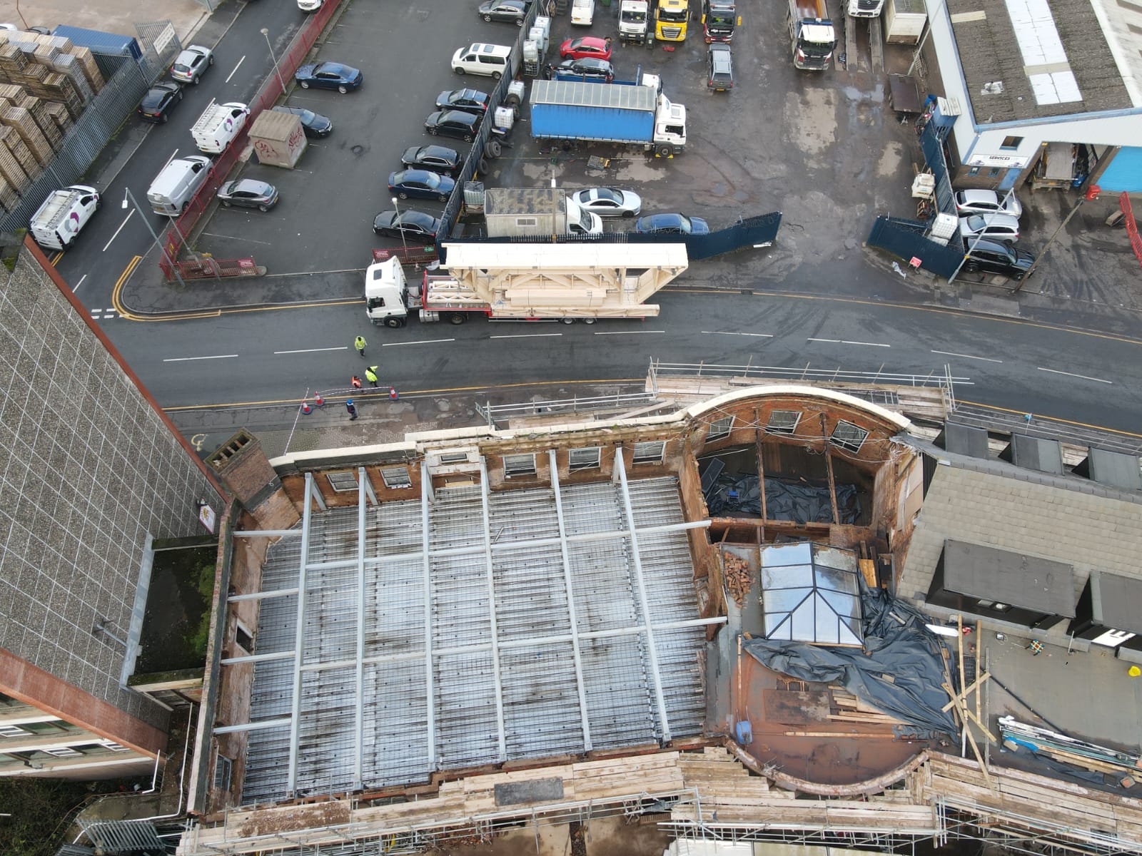 birds eye view of a building without a roof and a lorry delivering roof trusses behind