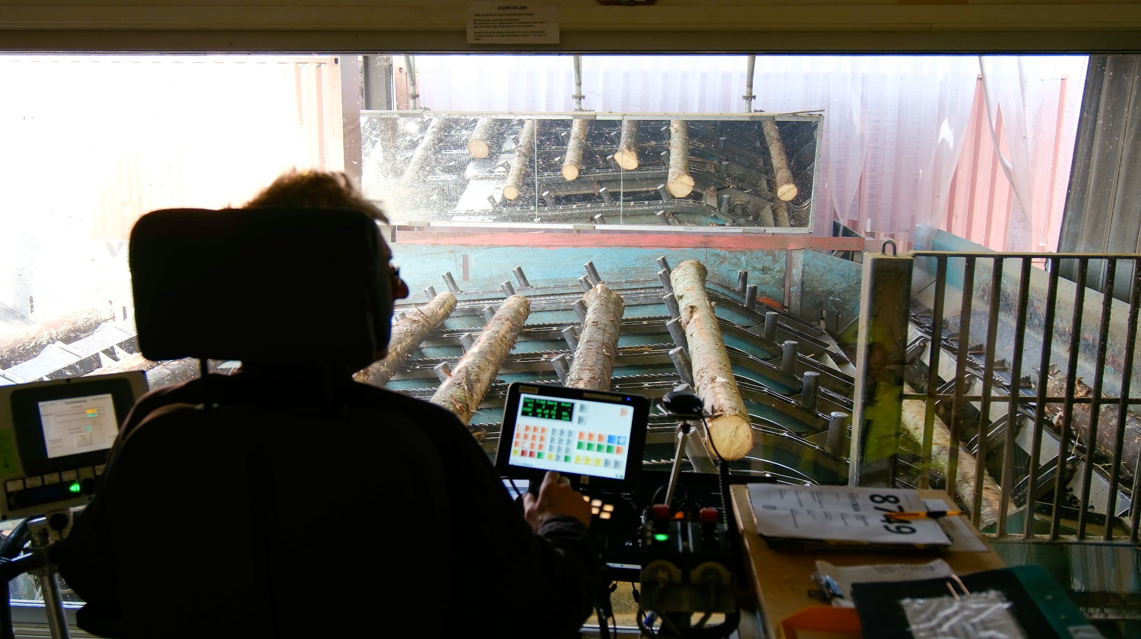 Person operating machinery in a control room with equipment and screens.