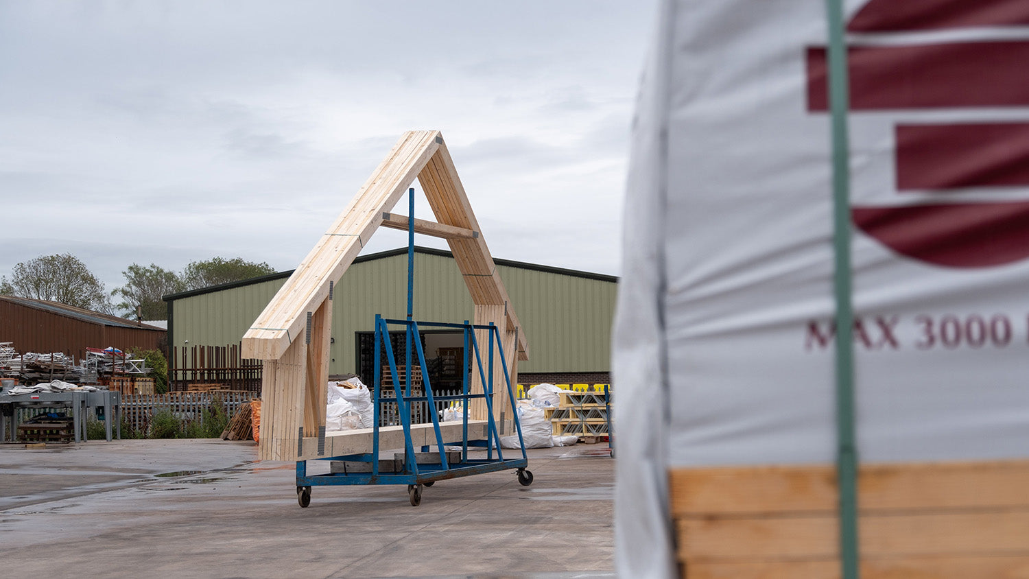 attic trusses on a trolley in a yard with a pack of timber in the foreground
