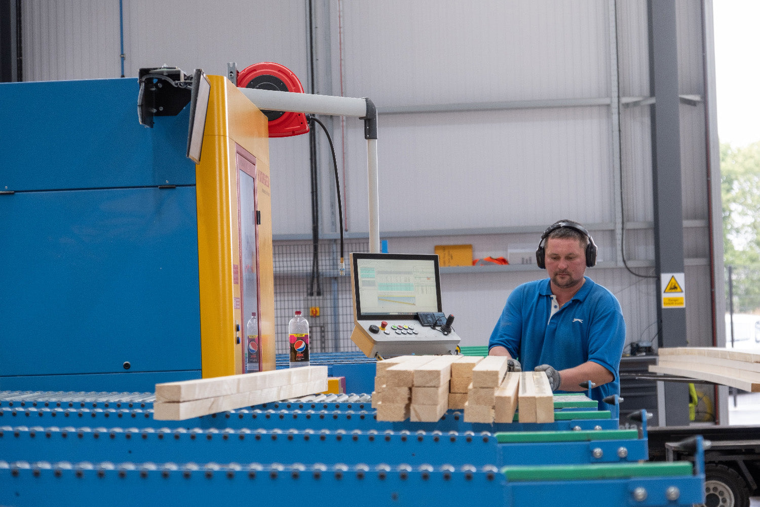 man wearing protective headphones cutting timber using a machine in a factory