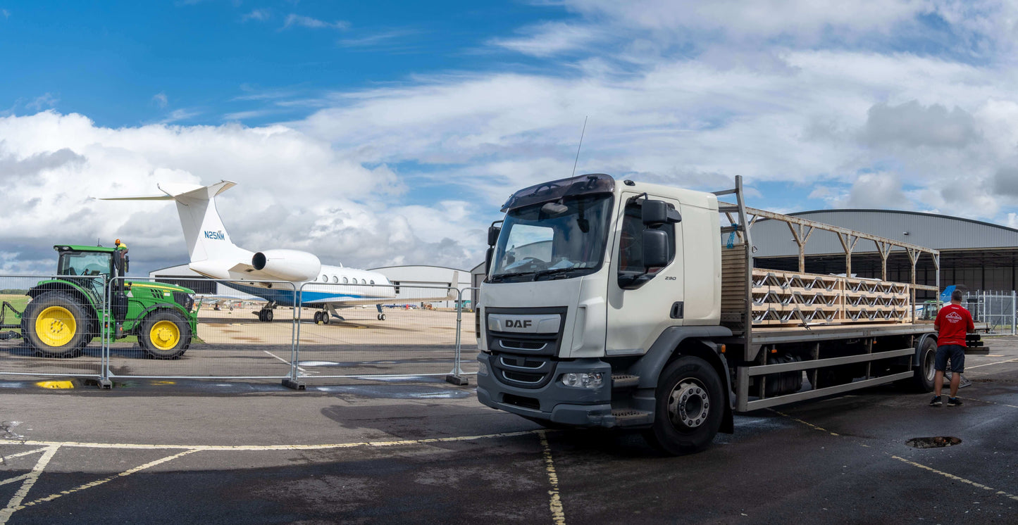 Truck with a trailer on an airport tarmac with a plane and tractor in the background.