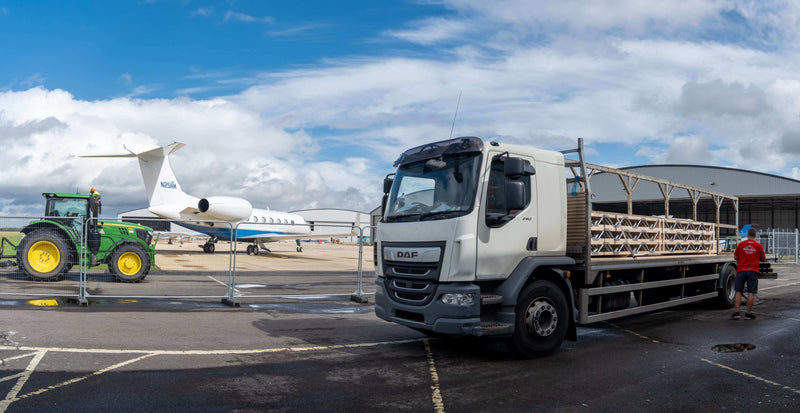 Truck with a trailer on an airport tarmac with a plane and tractor in the background in Oxfordshire