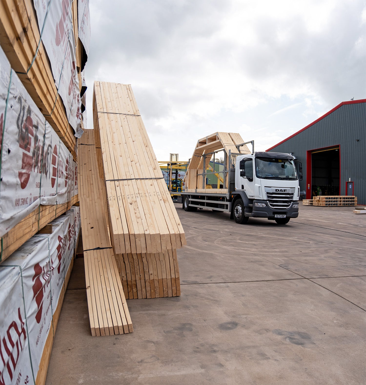 roof trusses stacked against packs of timber with a delivery lorry to the right