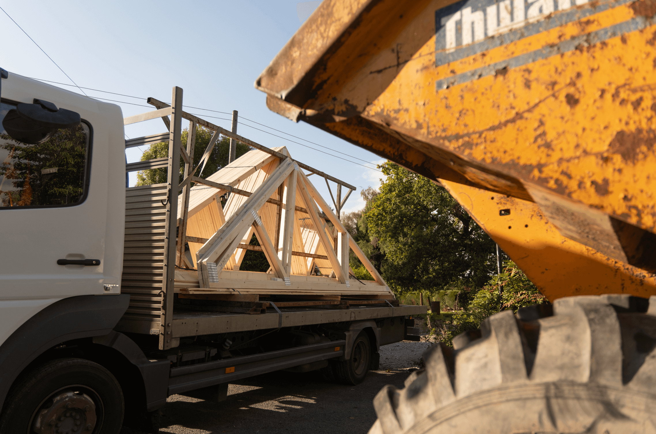 white lorry carrying fink trusses with a yellow machine in the foreground