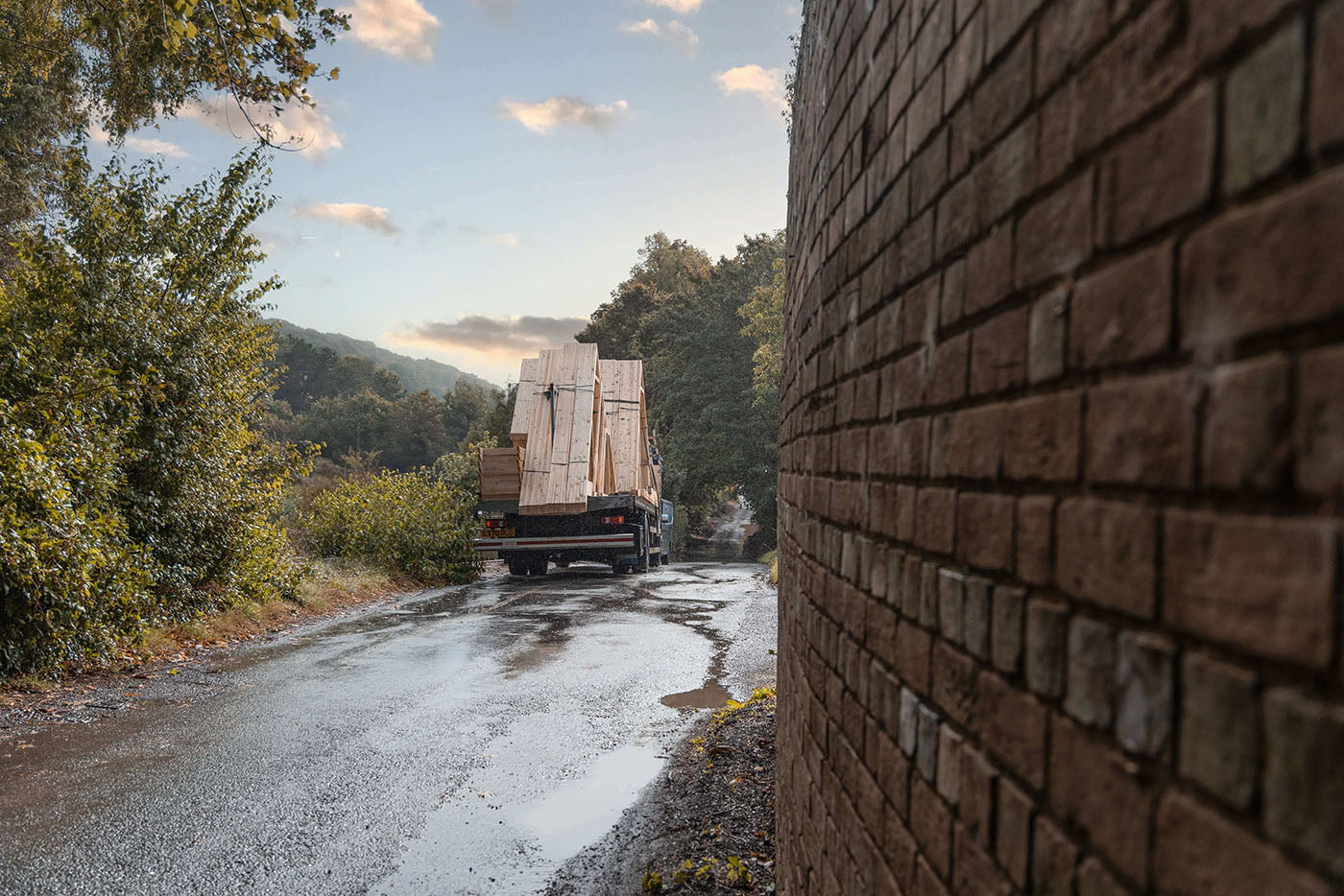 a lorry delivering roof trusses on a wet road with trees either side 