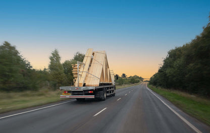 a flatbed lorry carrying roof trusses towards a sunrise